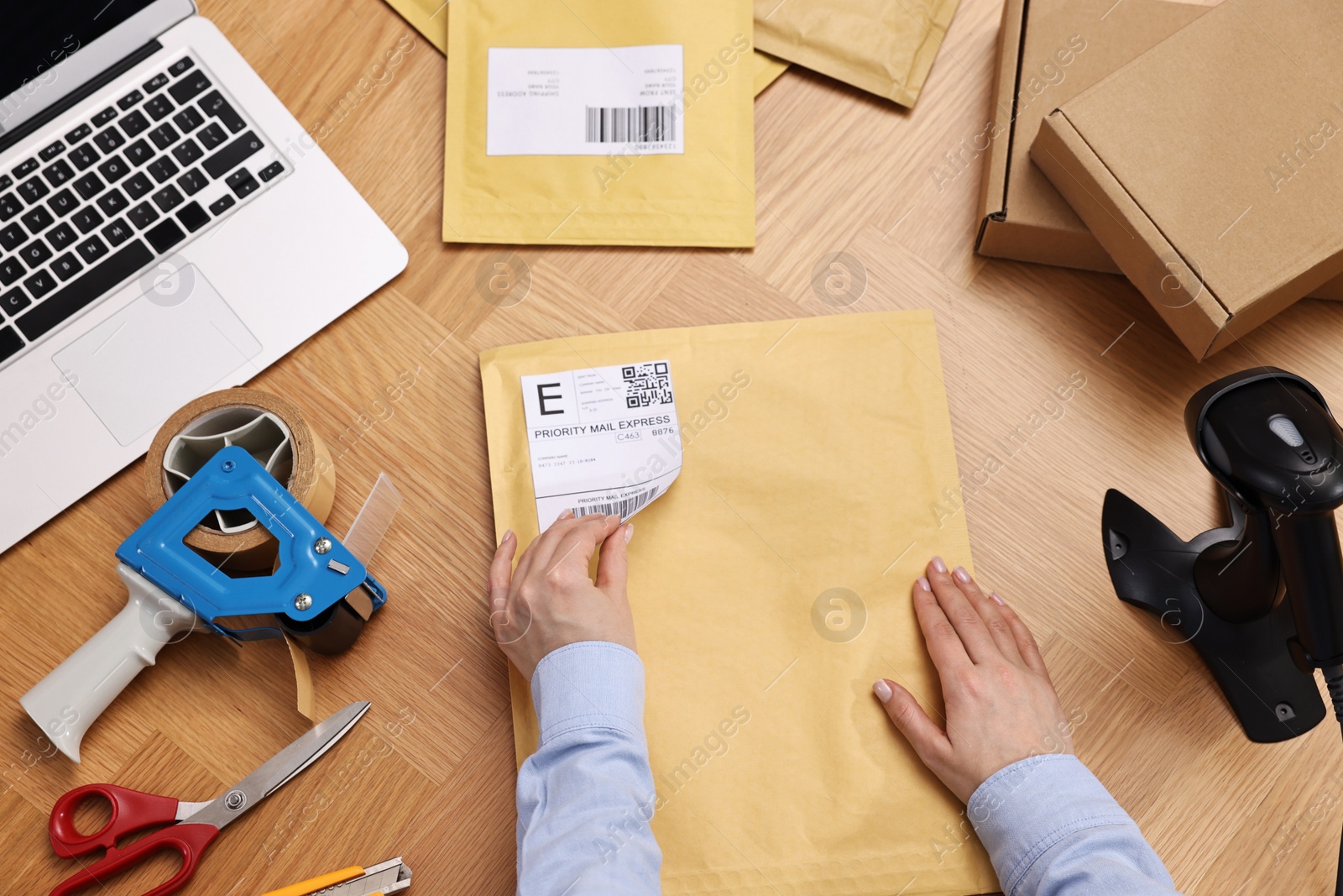 Photo of Parcel packing. Post office worker sticking barcode on bag at wooden table, top view