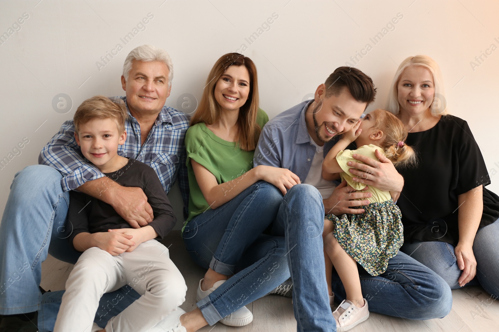 Photo of Happy family with cute kids sitting on floor near light wall