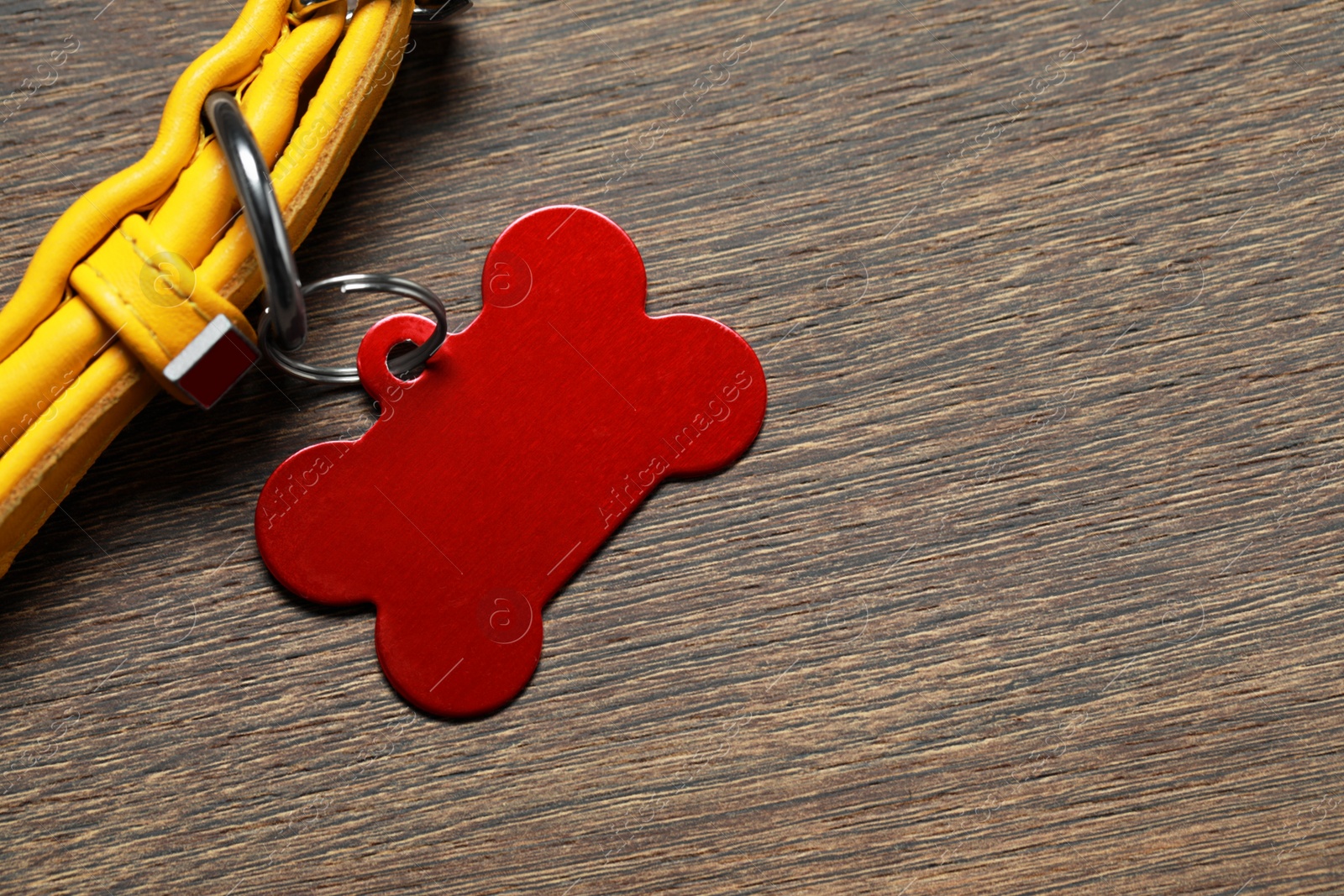 Photo of Yellow leather dog collar with red tag in shape of bone on wooden table, top view. Space for text