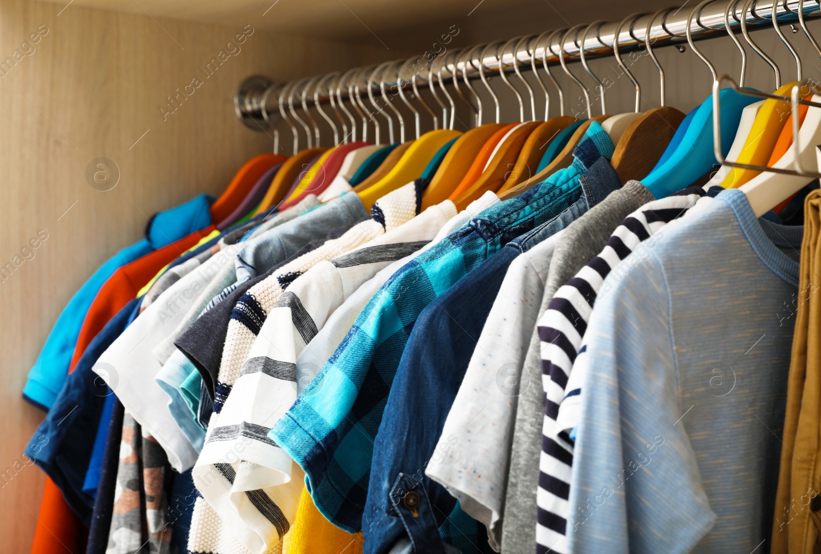 Photo of Hangers with teenage clothes on rack in wardrobe, closeup