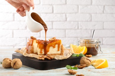 Woman pouring caramel sauce onto delicious pieces of cheesecake at wooden table, closeup