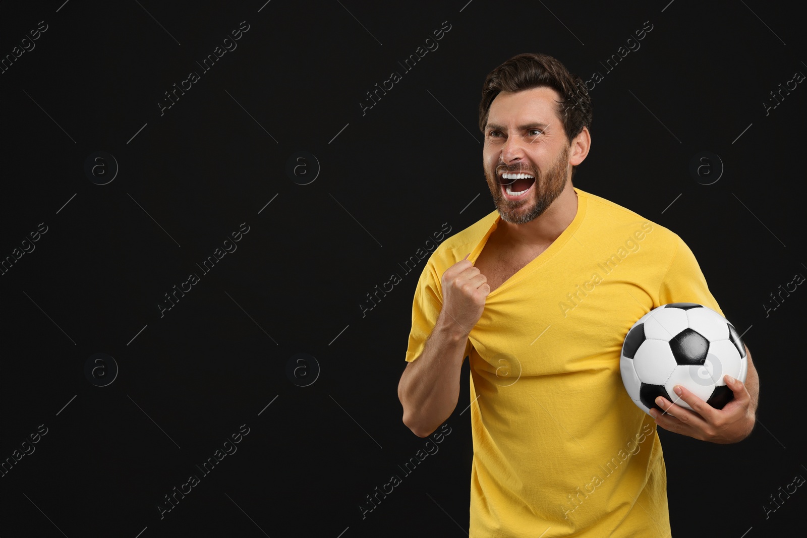 Photo of Emotional sports fan with soccer ball on black background, space for text