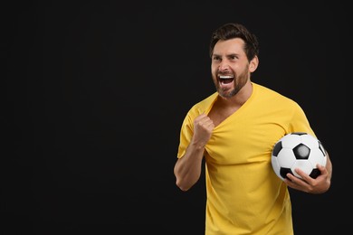 Photo of Emotional sports fan with soccer ball on black background, space for text