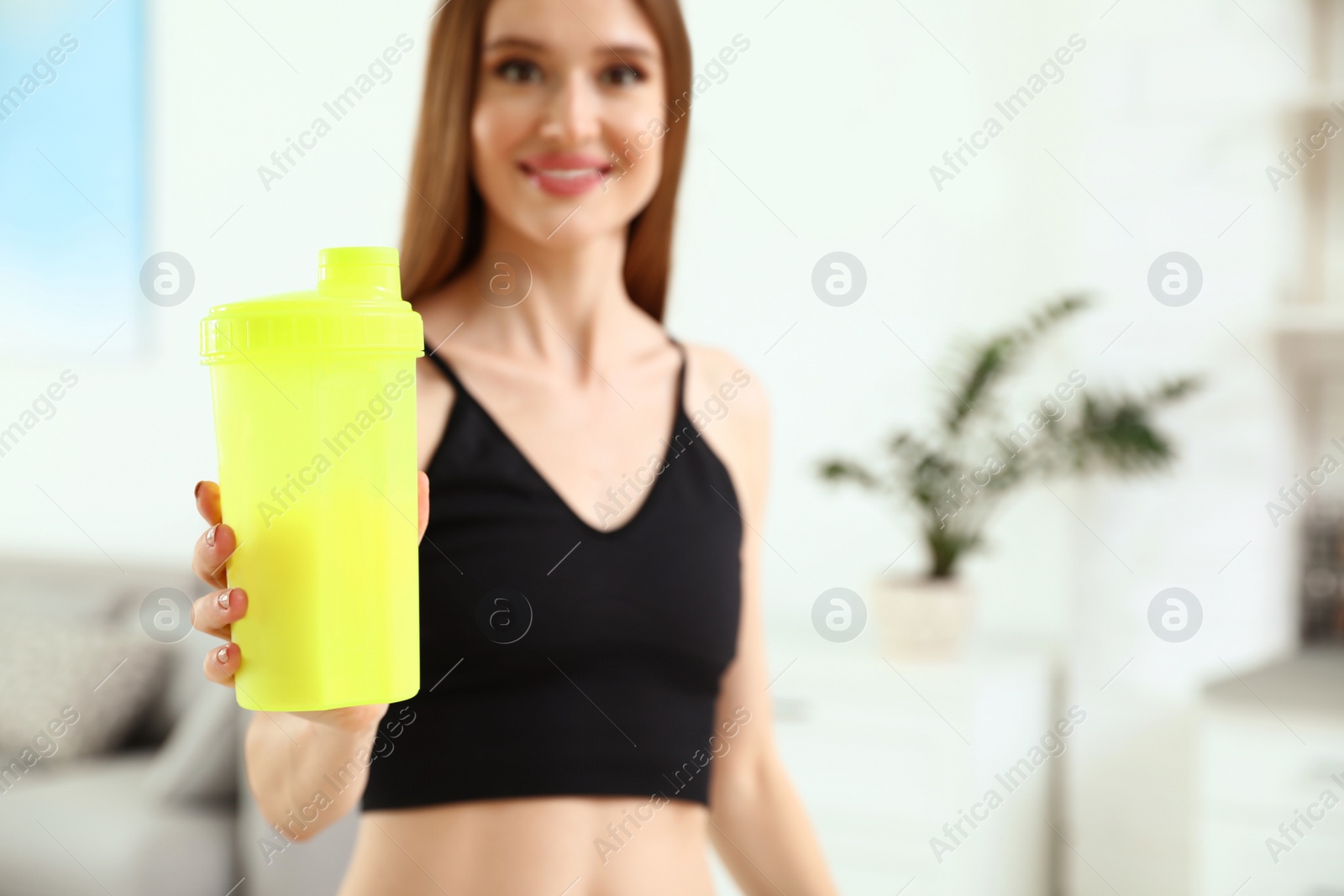 Photo of Young woman with bottle of protein shake at home. Space for text
