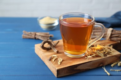 Photo of Aromatic licorice tea in cup and dried sticks of licorice root on blue wooden table, space for text