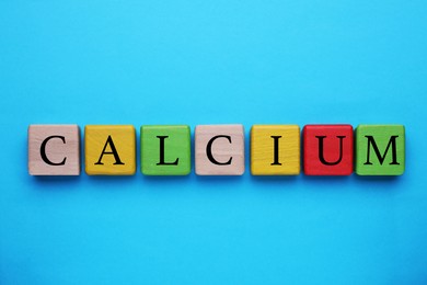 Word Calcium made of colorful wooden cubes with letters on light blue background, flat lay