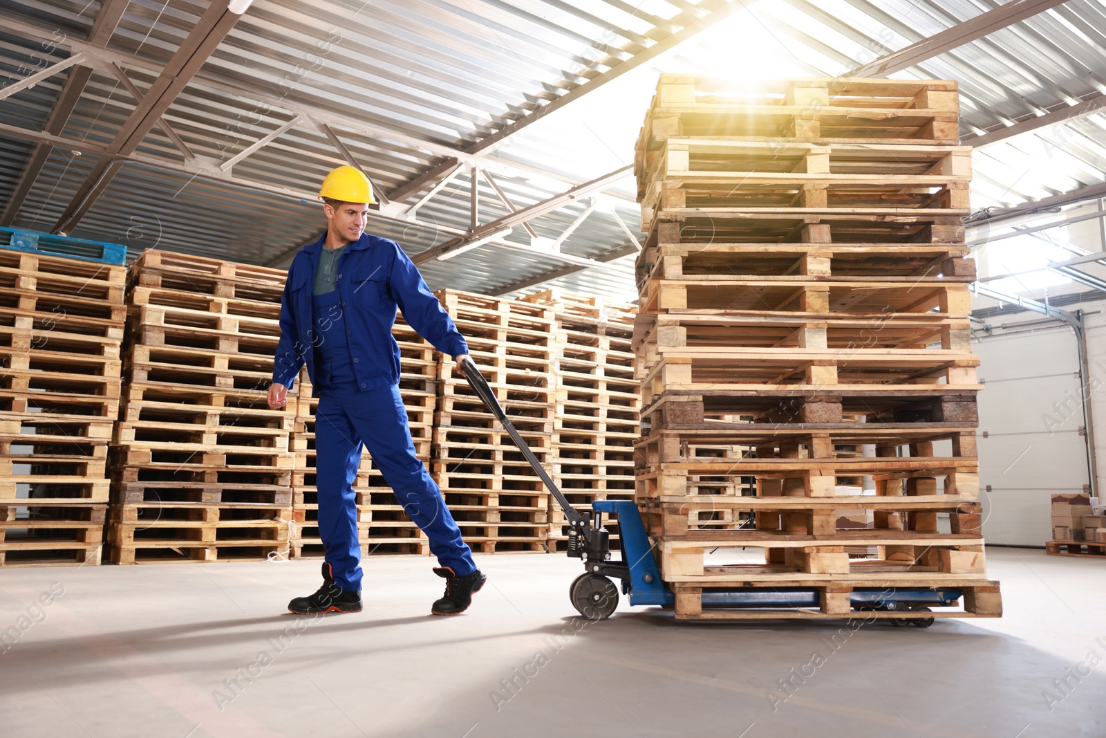 Image of Worker moving wooden pallets with manual forklift in warehouse