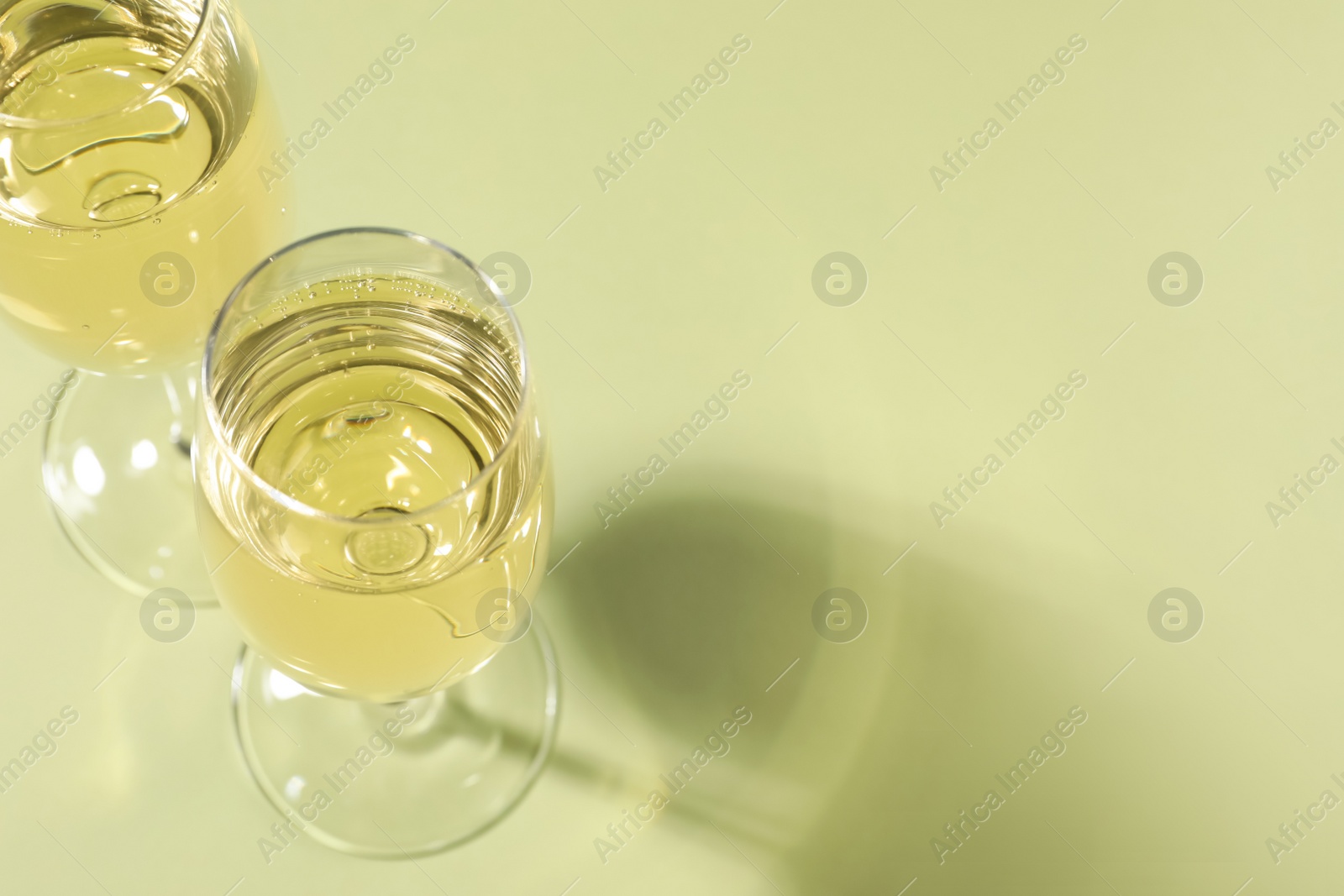 Photo of Glasses of delicious sparkling wine on light yellow background, above view. Space for text