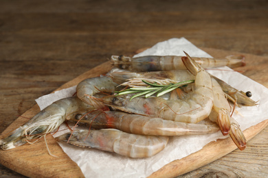Photo of Fresh raw shrimps with rosemary on wooden table