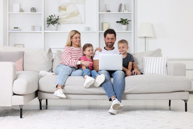 Photo of Happy family with laptop spending time together on sofa at home