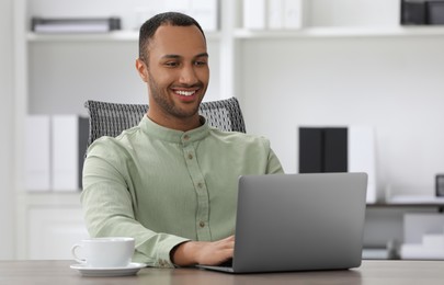 Photo of Handsome young man with laptop at table in office