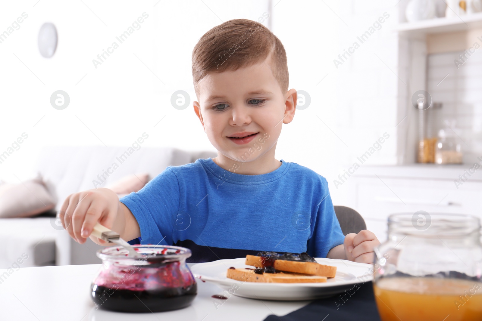 Photo of Cute little boy spreading sweet jam onto toast at table