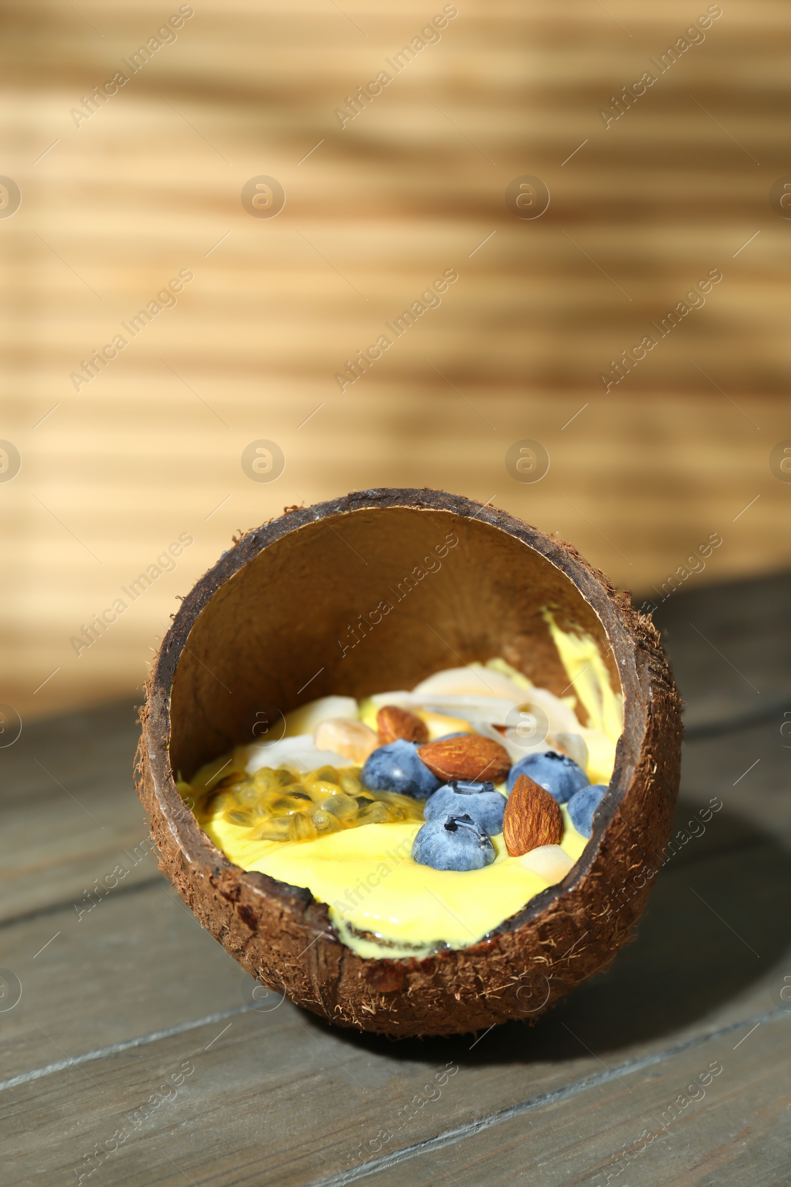 Photo of Tasty smoothie bowl with fresh blueberries and almonds served in coconut shell on wooden table