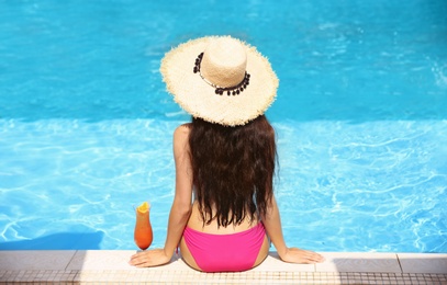 Photo of Young woman with cocktail sitting near swimming pool