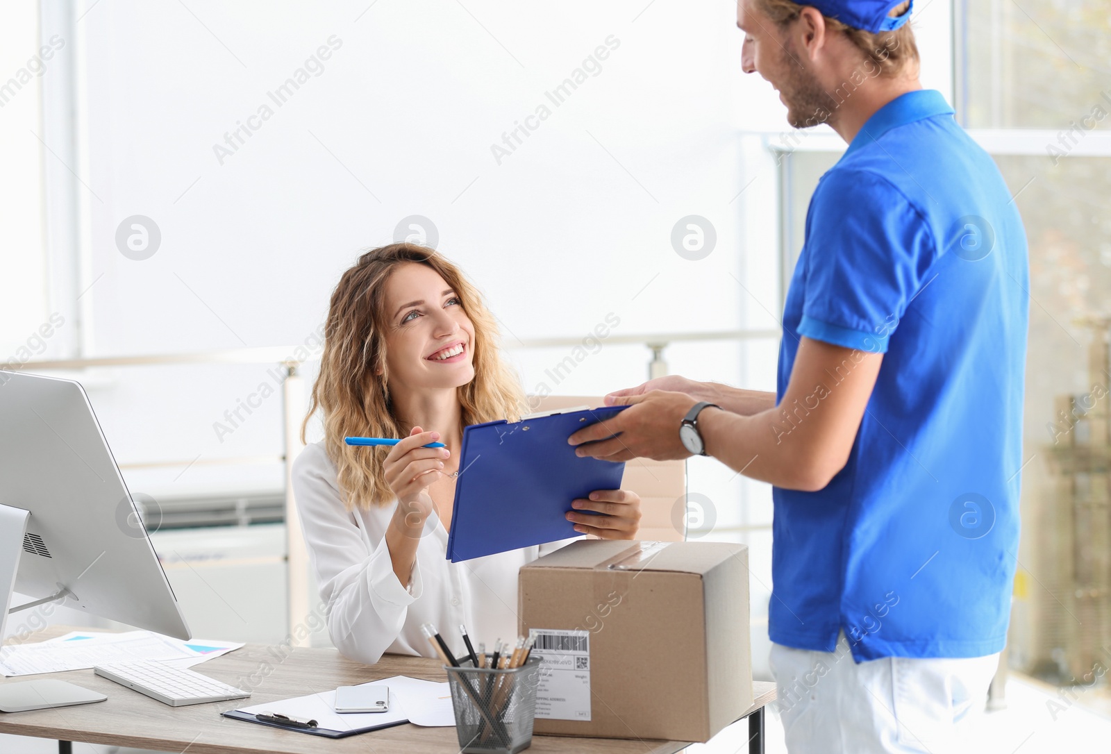 Photo of Young woman signing for delivered parcel in office. Courier service