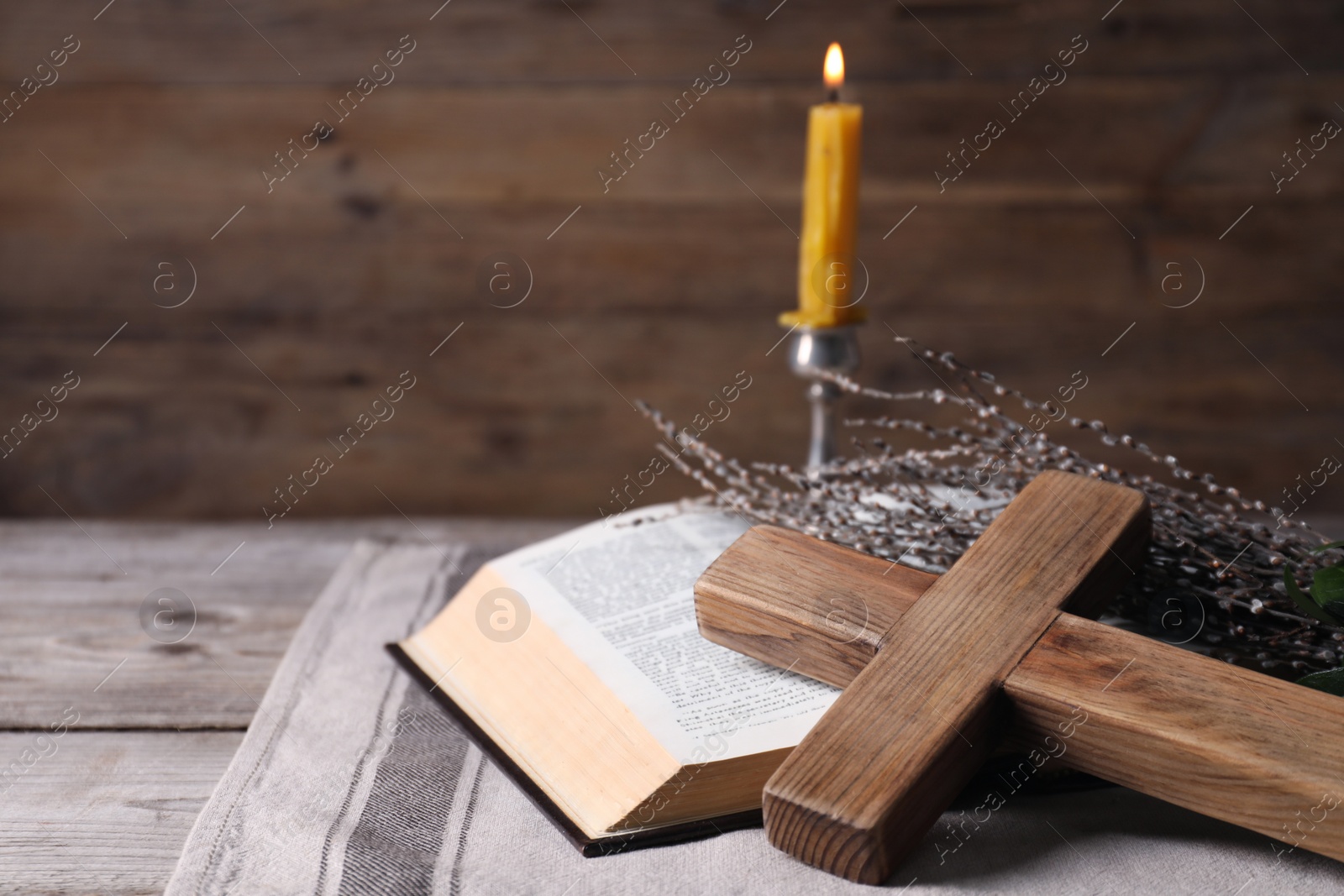 Photo of Cross, Bible, willow branches and burning candle on wooden table, space for text