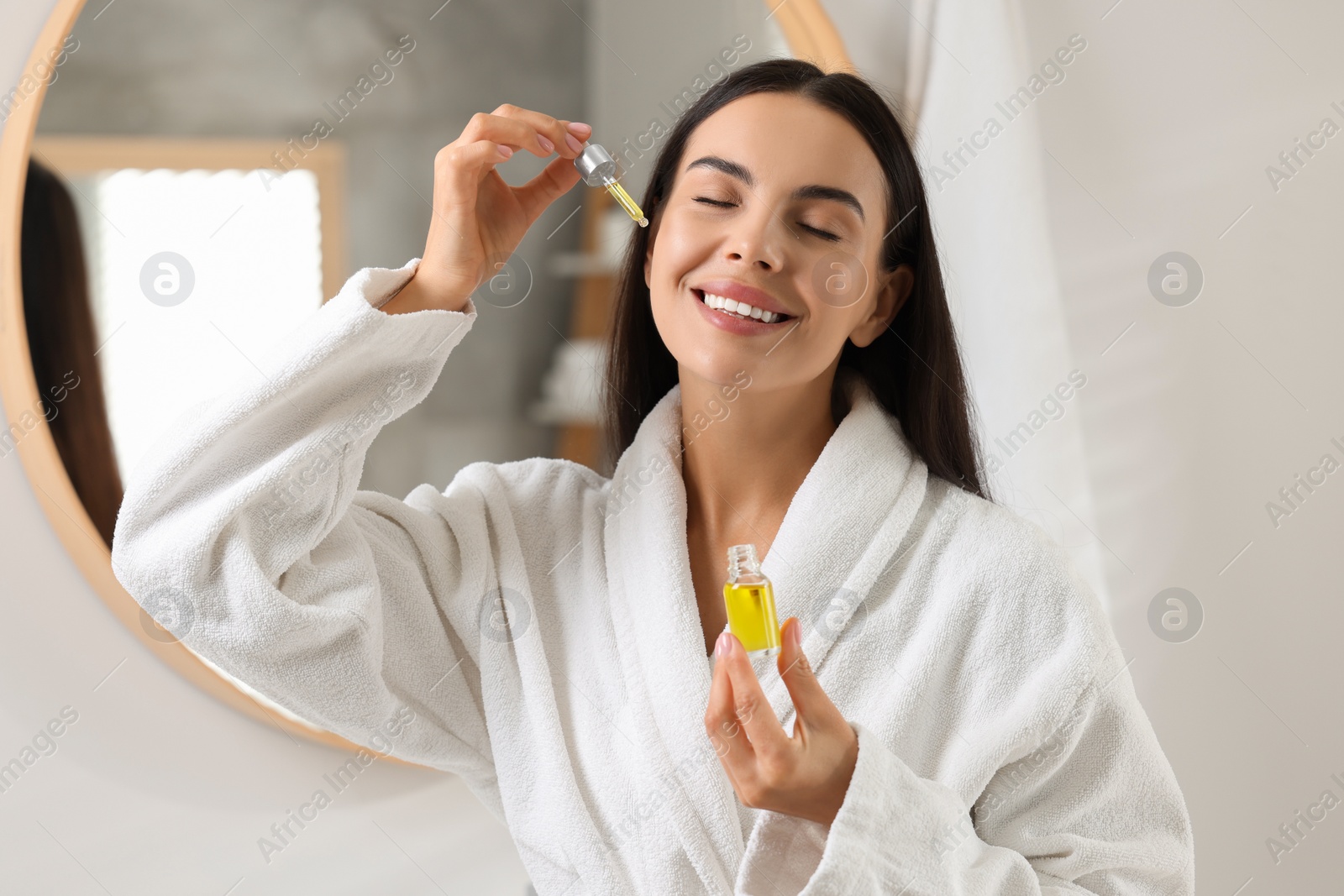 Photo of Beautiful young woman applying serum onto her face in bathroom