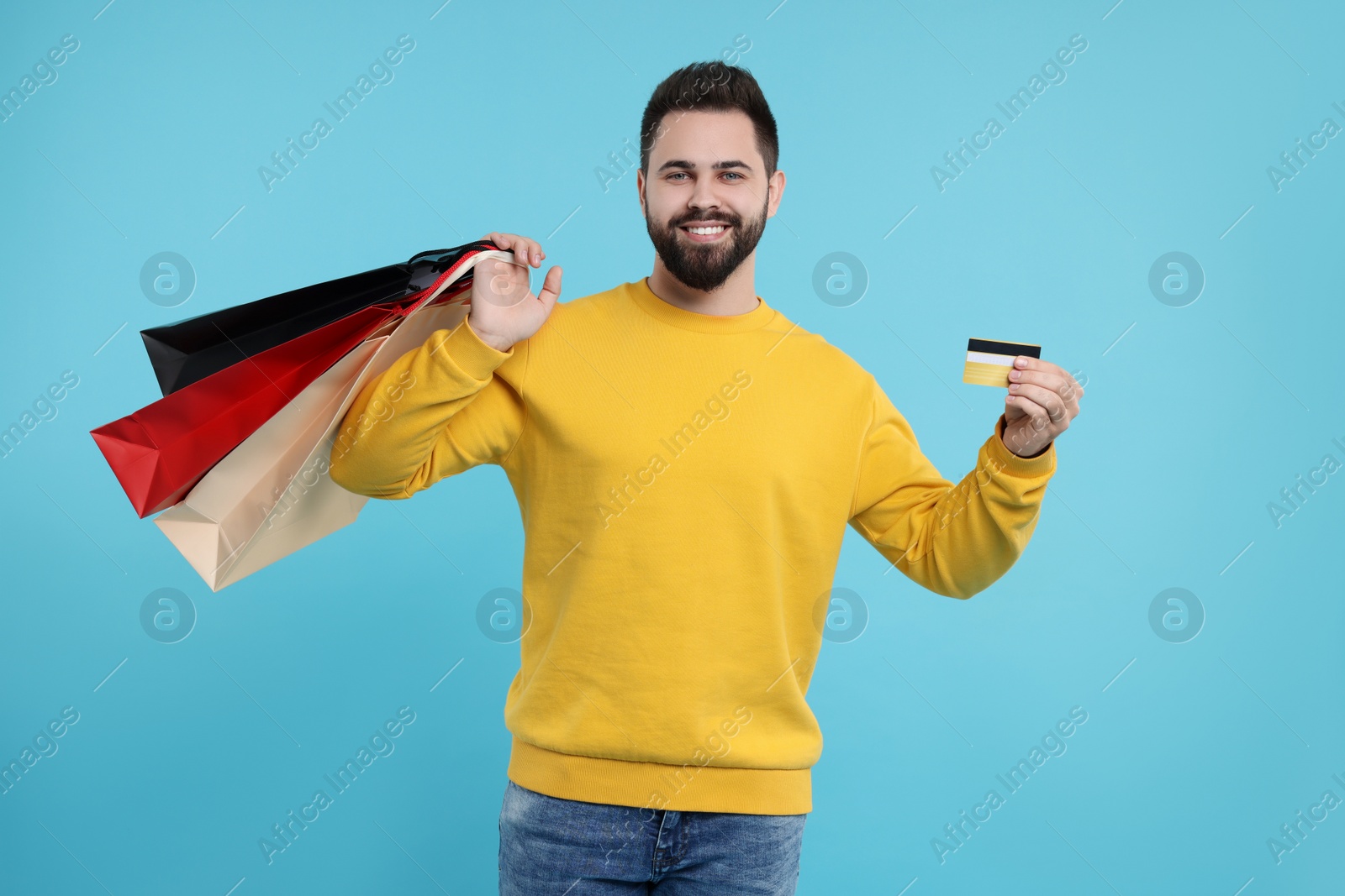 Photo of Smiling man with paper shopping bags showing credit card on light blue background