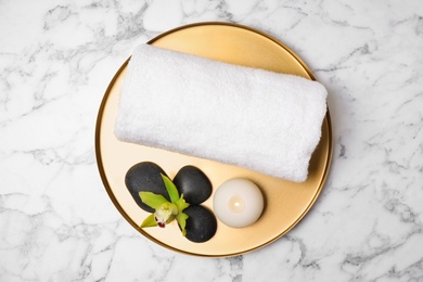 Tray with towel and spa stones on white marble table, top view
