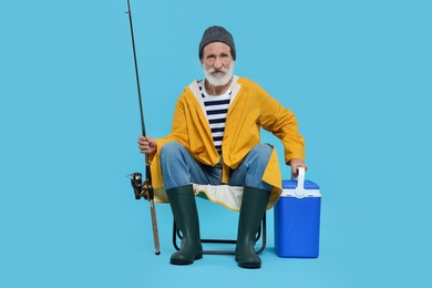 Fisherman with rod and cool box on chair against light blue background