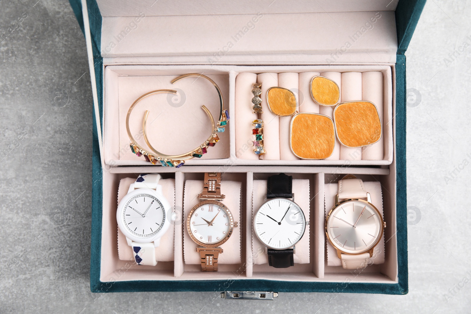 Photo of Elegant jewelry box with beautiful bijouterie and expensive wristwatches on light grey stone table, top view