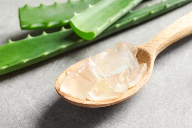 Spoon with peeled aloe vera and green leaves on gray background