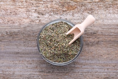 Glass bowl with dried thyme and scoop on wooden table, top view