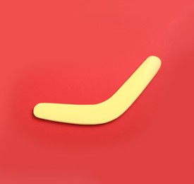 Photo of Yellow wooden boomerang on red background, top view