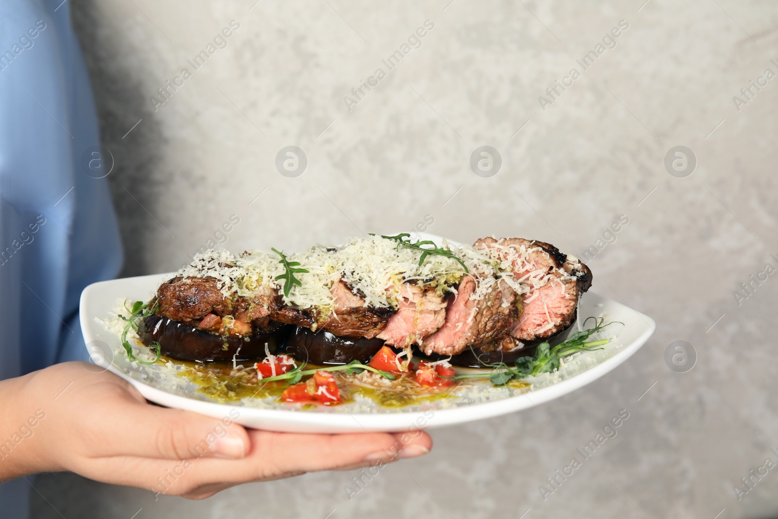 Photo of Woman holding plate with delicious roasted meat on grey background, closeup