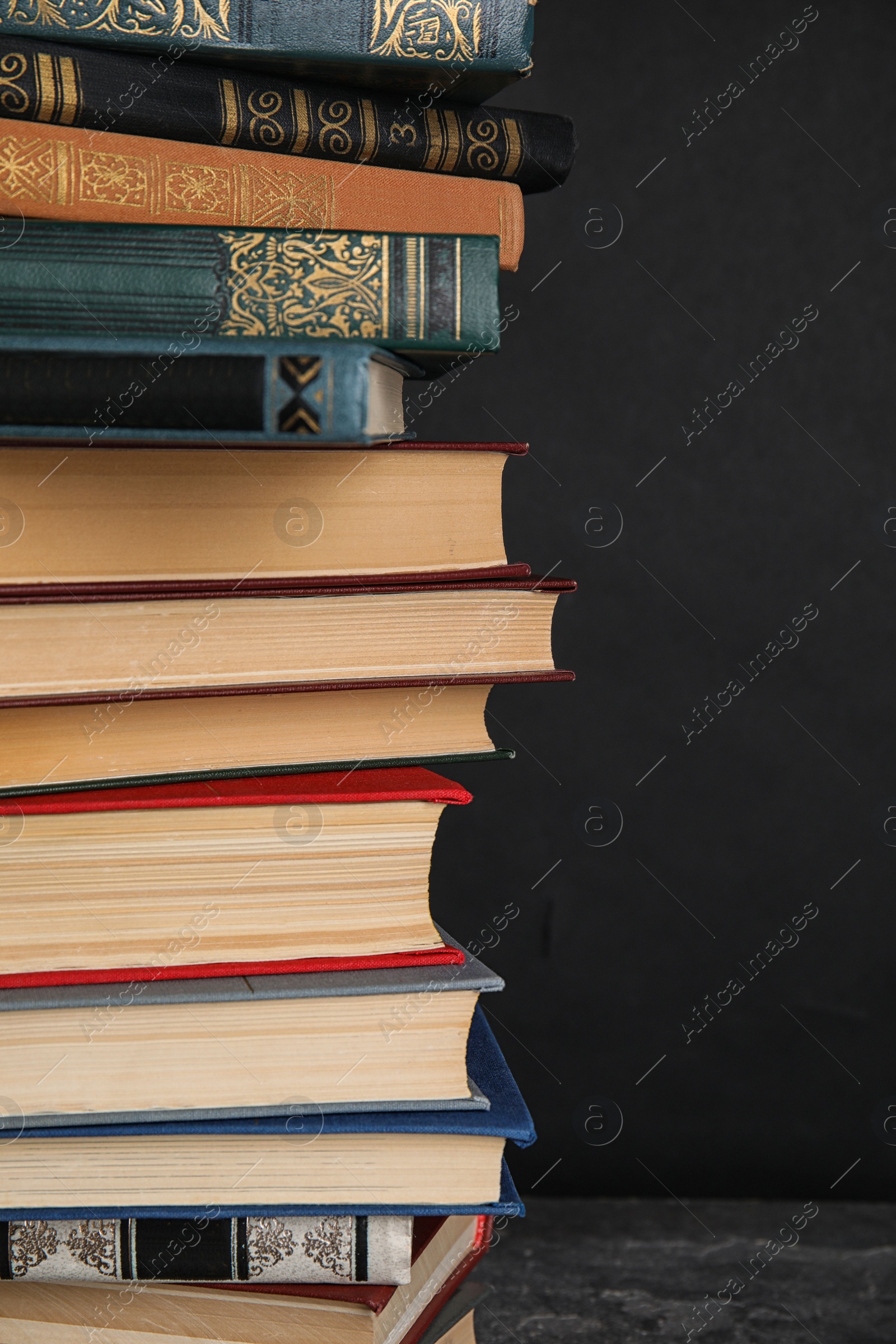 Photo of Stack of hardcover books on grey stone table against black background