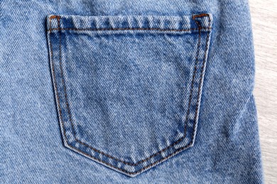 Stylish light blue jeans on white wooden background, closeup of back pocket