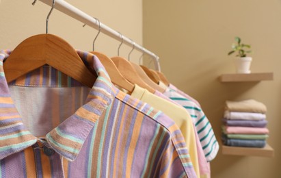 Photo of Wooden hangers with stylish clothes on rack near beige wall. Dressing room interior