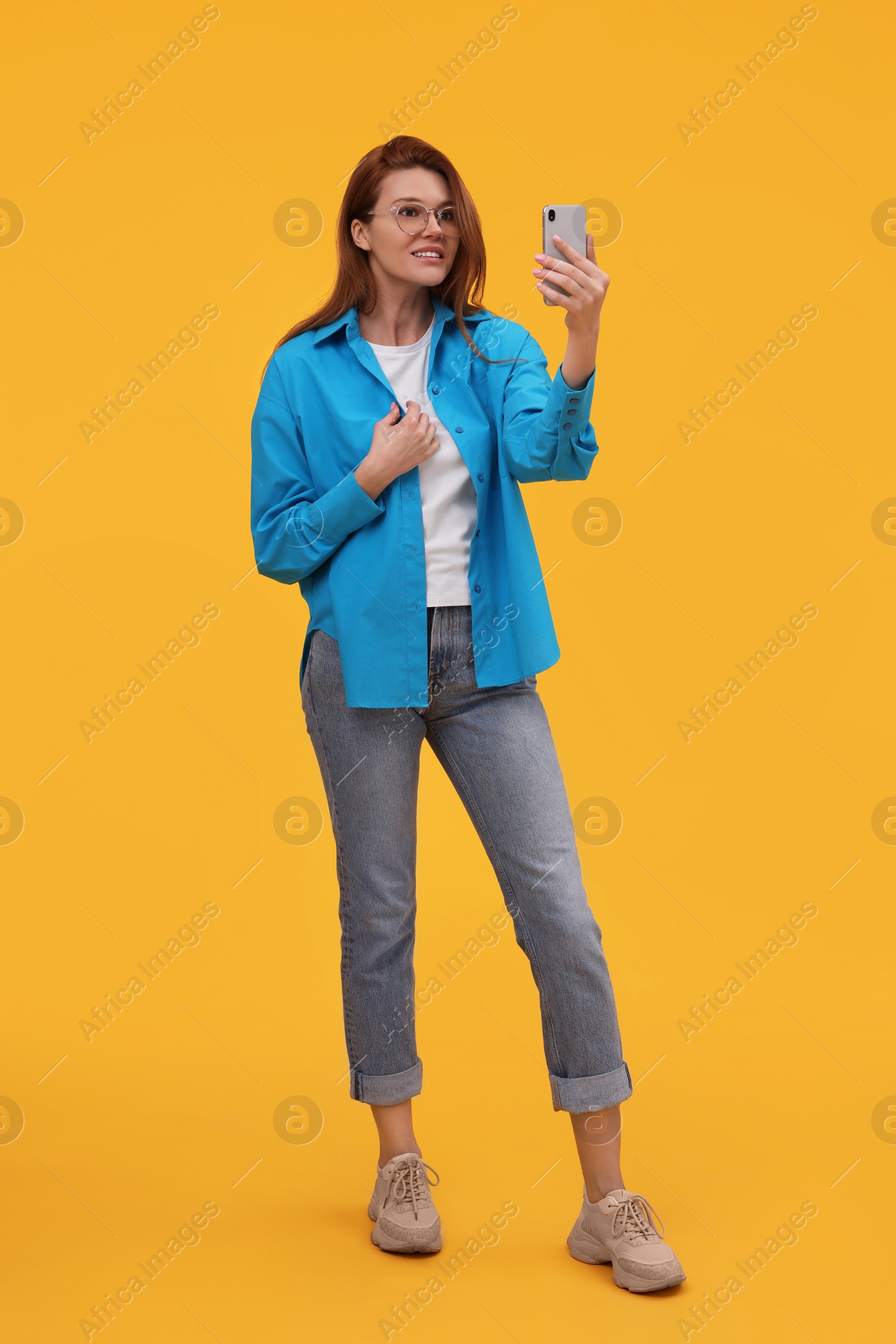 Photo of Beautiful woman in eyeglasses taking selfie on orange background