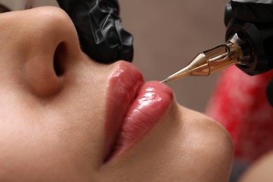Photo of Young woman undergoing procedure of permanent lip makeup in tattoo salon, closeup