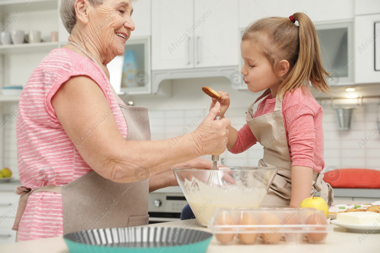 Photo of Cute girl and her grandmother cooking in kitchen