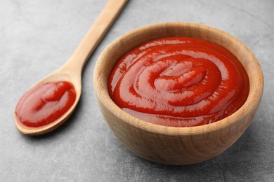 Photo of Bowl and spoon of tasty ketchup on light grey table, closeup