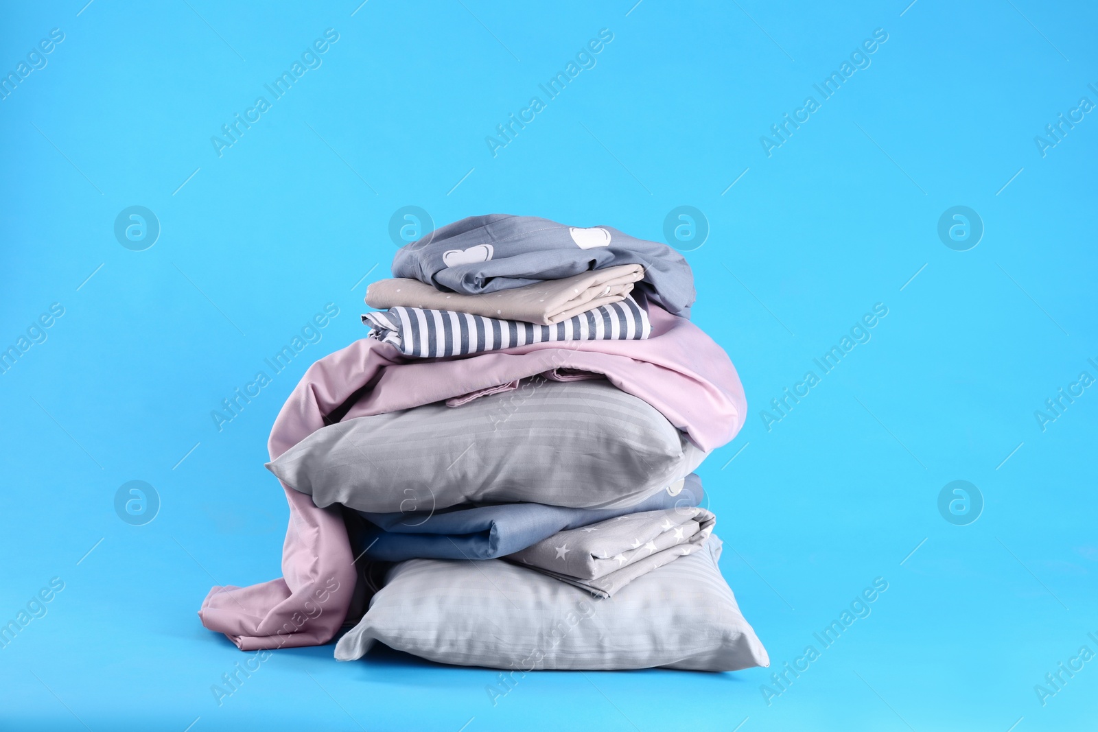 Photo of Stack of clean bed sheets and pillows on blue background