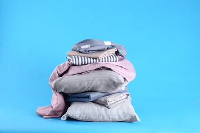 Photo of Stack of clean bed sheets and pillows on blue background