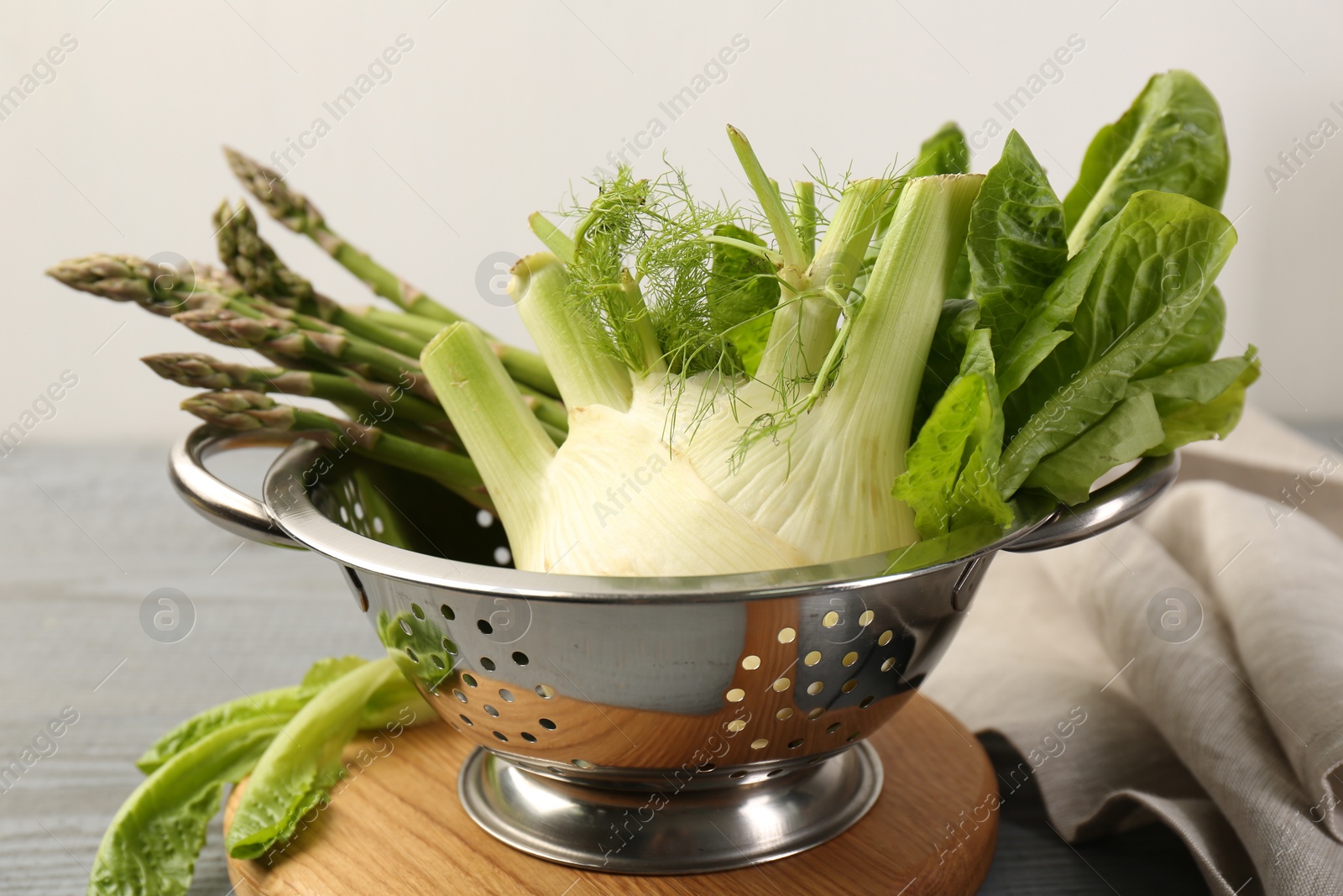 Photo of Metal colander with fennel, lettuce and asparagus on table, closeup