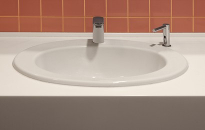 Photo of Clean ceramic sink near tiled wall in public toilet