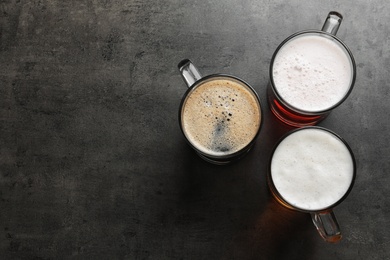 Glass mugs with different types of cold tasty beer on grunge background, top view