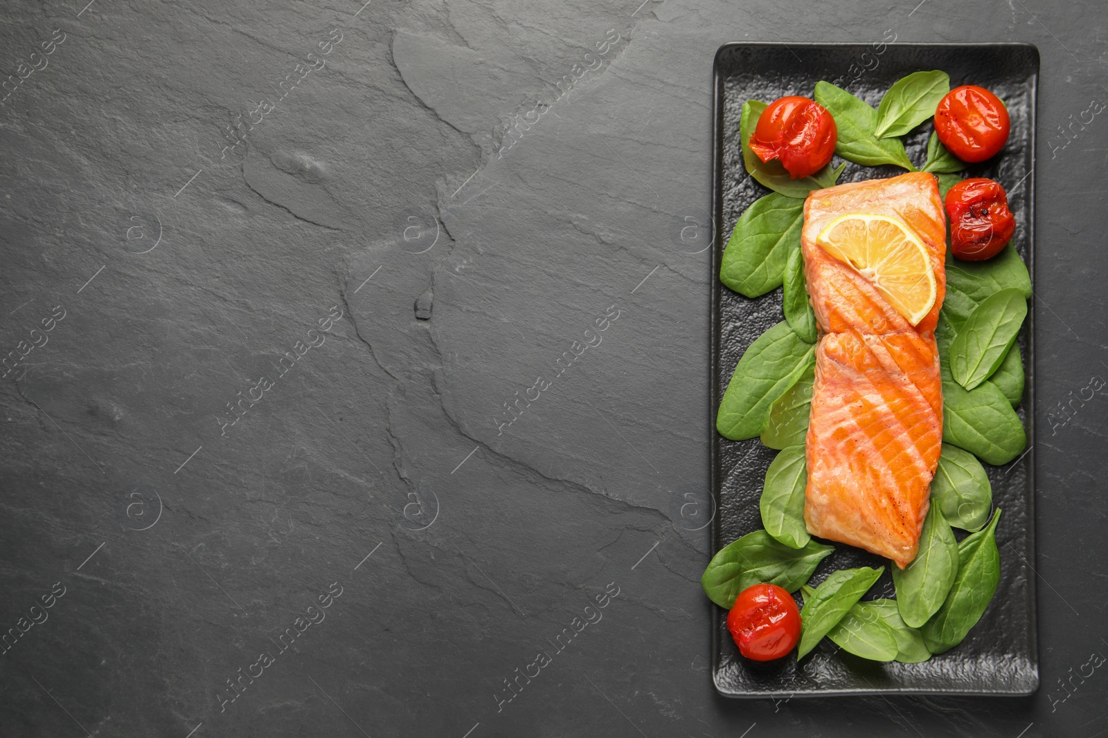 Photo of Tasty grilled salmon with tomatoes, spinach and lemon on black table, top view. Space for text