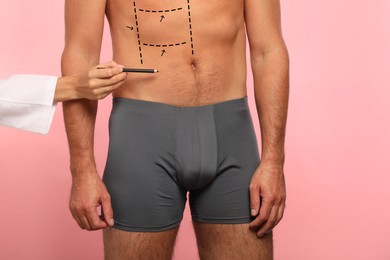 Image of Man preparing for cosmetic surgery, pink background. Doctor drawing markings on his abdomen, closeup