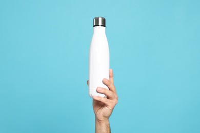 Photo of Man holding thermo bottle on light blue background, closeup