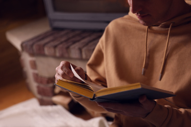 Man reading book near fireplace at home, closeup