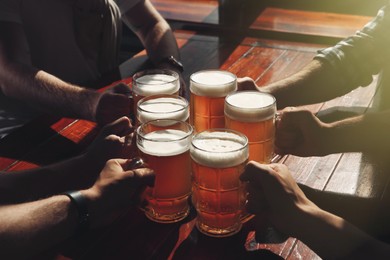 Photo of Friends clinking glasses with beer at table, closeup