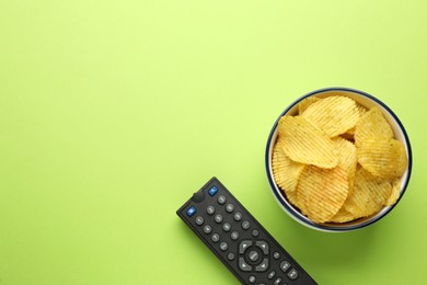 Photo of Remote control and bowl of potato chips on light green background, flat lay. Space for text