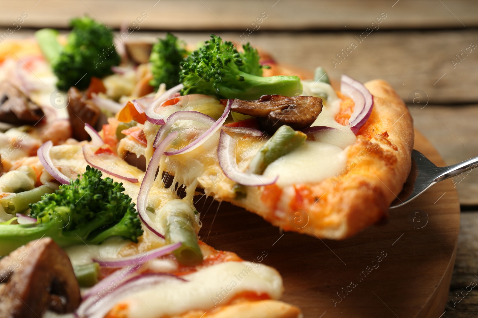 Photo of Taking piece of delicious vegetarian pizza at wooden table, closeup