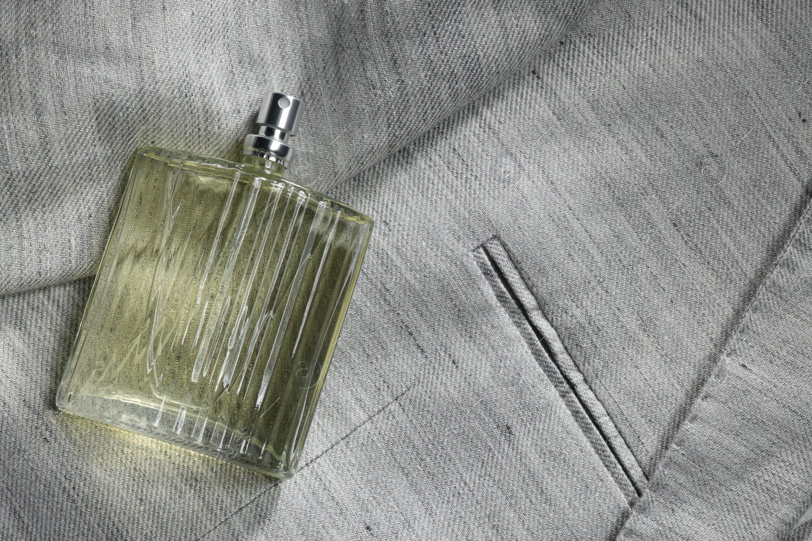 Photo of Luxury men's perfume in bottle on grey jacket, top view. Space for text