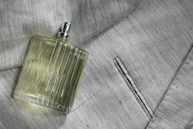 Photo of Luxury men's perfume in bottle on grey jacket, top view. Space for text